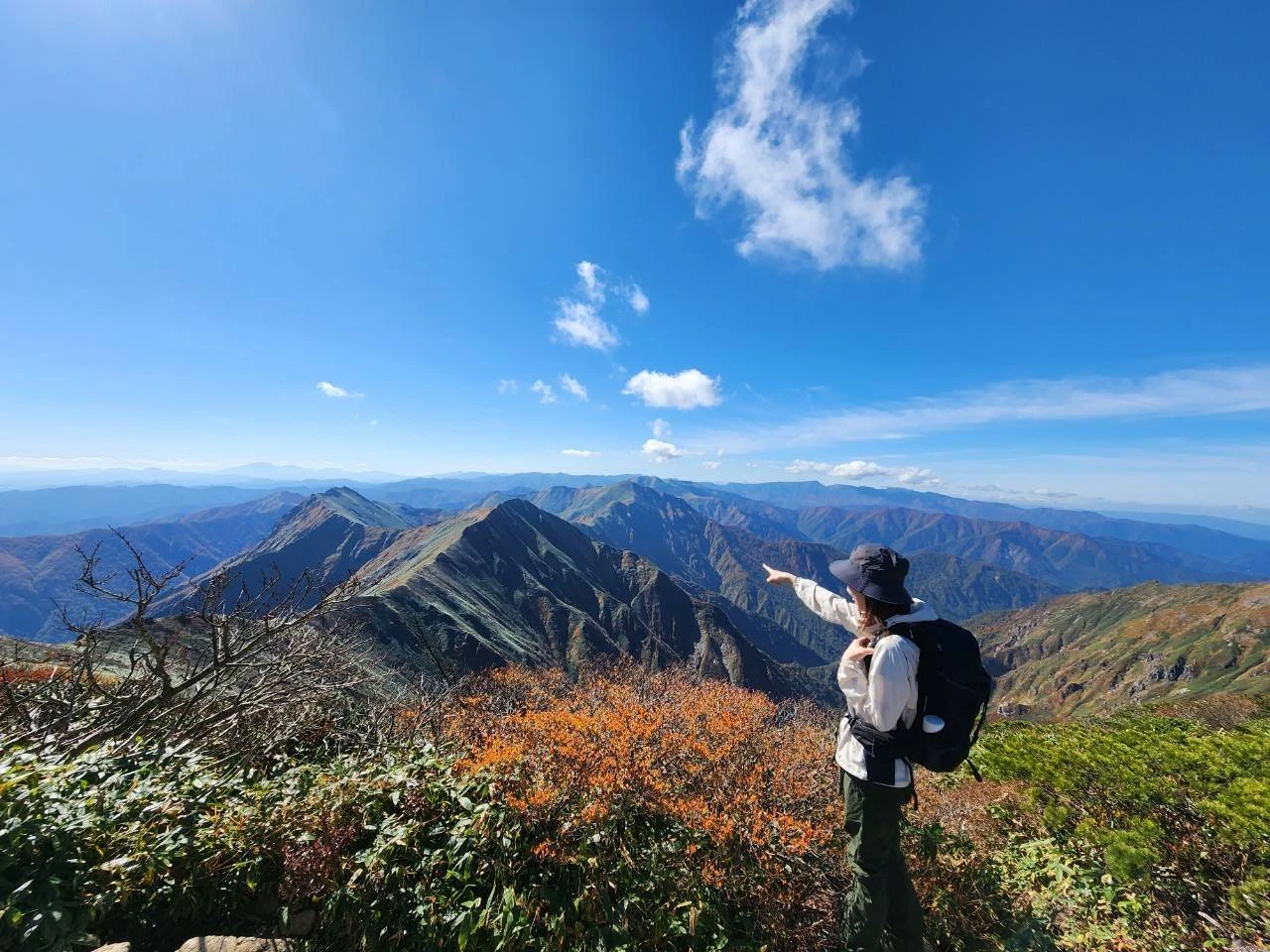 秋の山の尾根で、遠くの山並みを指さしている仙石